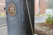 A bronze replica of Donnie Eagles' broom, created by Brenda Wainman Goulet, rests against the entrance to River Mill Park