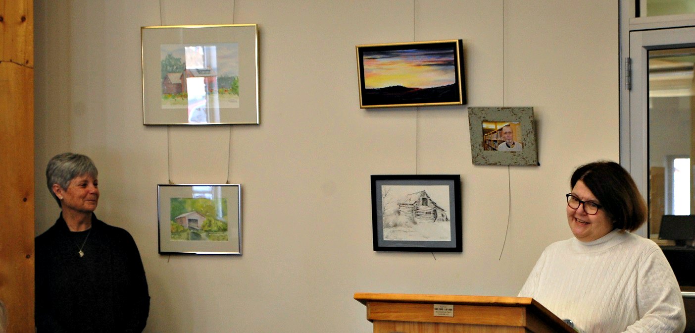 Chief Librarian Deb Duce (right) thanks the Tappin family for their donation of art (hanging in the background) in memory of Nigel Tappin, with library board member Sue Morris (left)