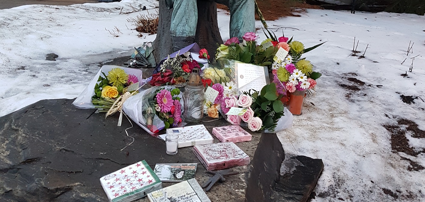 Flowers and other items left in memory of Brenda Wainman Goulet at the foot of the Tom Thomson statue she created
