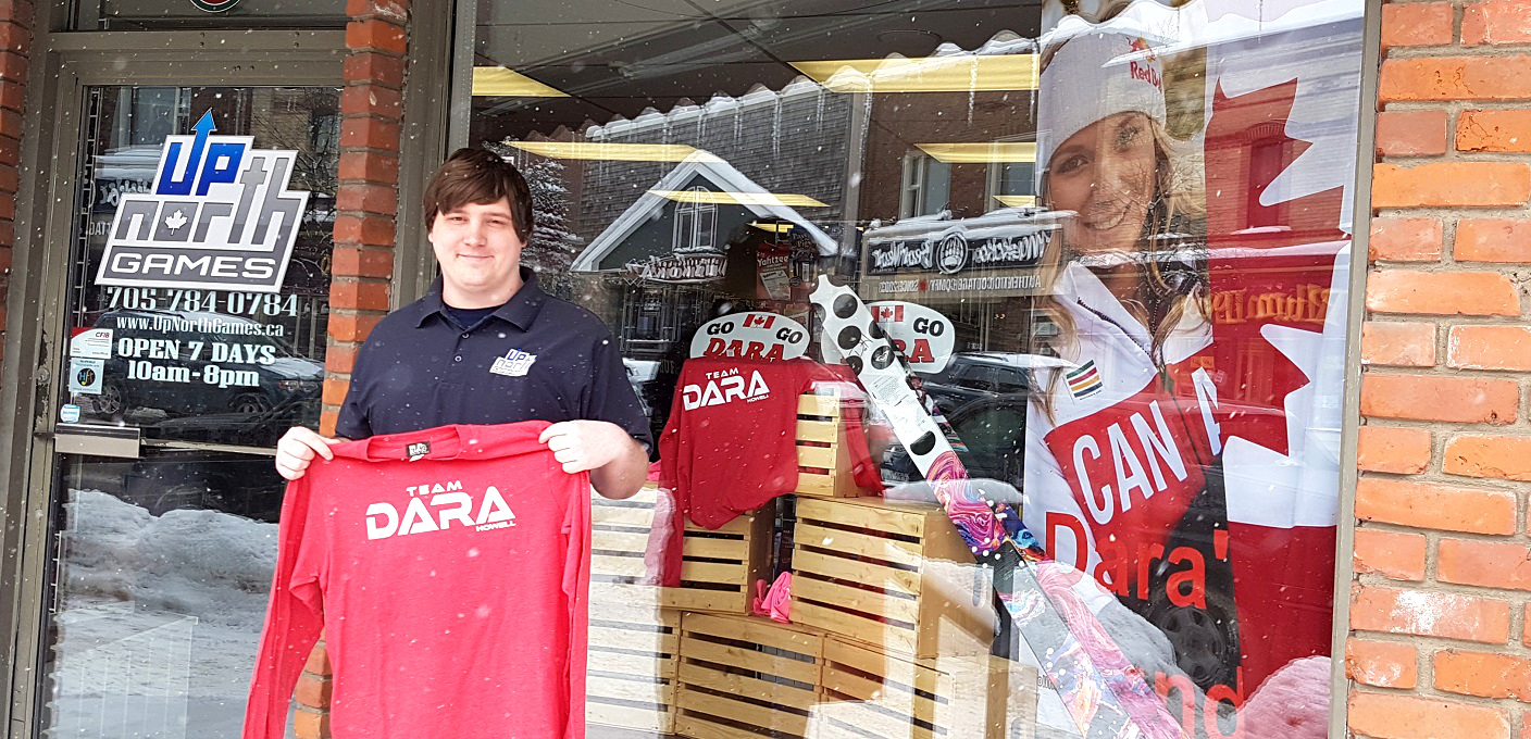 Kade Nelson holds up a Team Dara shirt in front of Up North Games