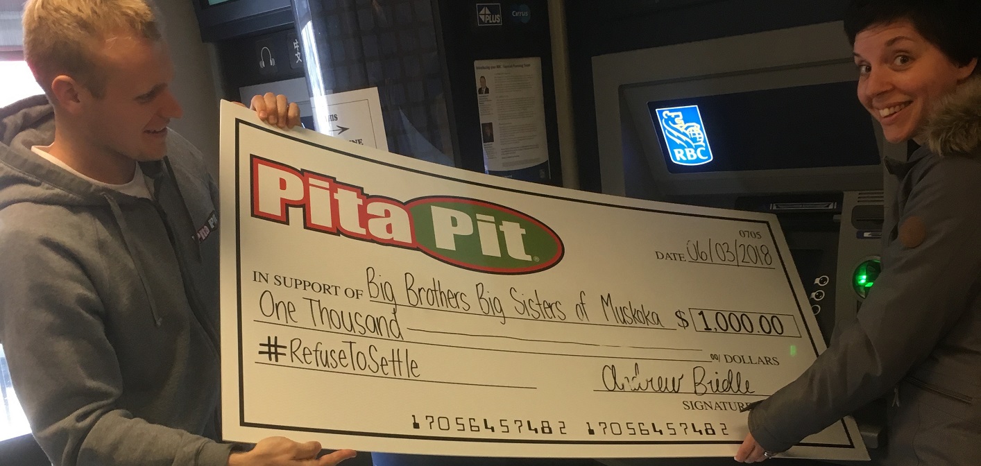 Andrew Bridle (left) of Pita Pit and Rebecca Paul, Executive Director of Big Brothers Big Sisters Muskoka ‘deposit’ a $1,000 donation to the organization (supplied photo)