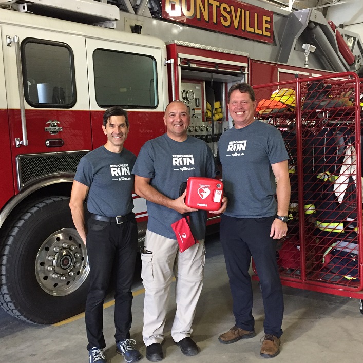 Dr. Lowell Grieb of The SportLab (left) and Roger Hennig of Save Station (right) present Huntsville firefighter Paul Calleja with an automated external defibrillator (Photo: The SportLab)