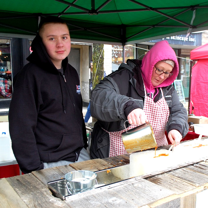 Sherri Campbell (right) of Sweetwater Maple Syrup pours maple syrup over ice blocks while Jayden Campbell waits to twirl it onto a stick to satisfy the sweet-tooths of festival attendees