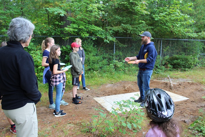 Disc golfer Tom Cowan on tee pad 4 with grade 7/8 students