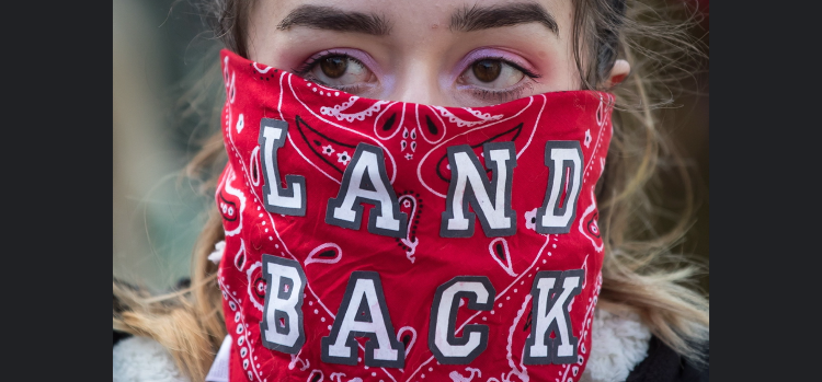 A woman wears a bandana over her face reading ‘Land Back’ at a protest march in support of Wet’suwet’en Nation hereditary chiefs. (THE CANADIAN PRESS/Darryl Dyck)