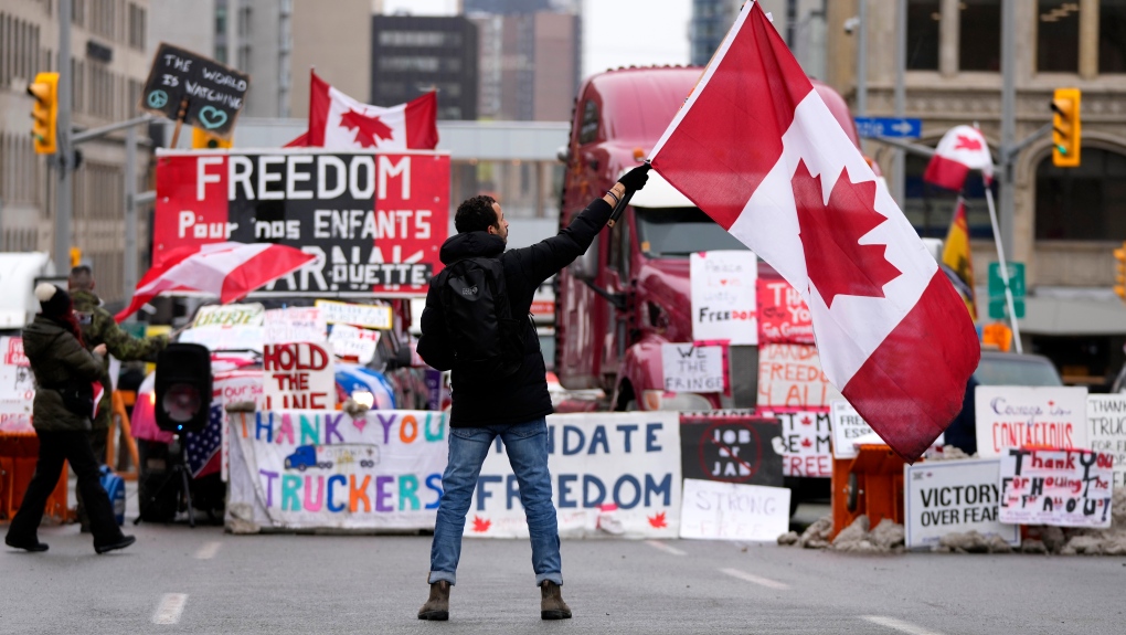 A protester waves a Canadian flag in front of parked vehicles on Rideau Street in Ottawa on Friday, Feb. 11, 2022. (THE CANADIAN PRESS/Justin Tang)